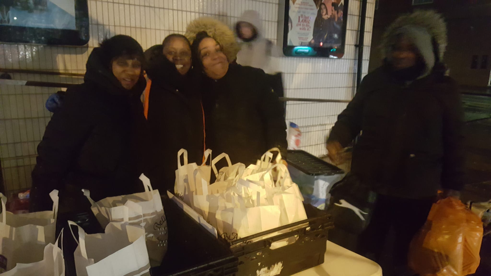 Photograph of volunteers smiling at the camera, giving away food bags.