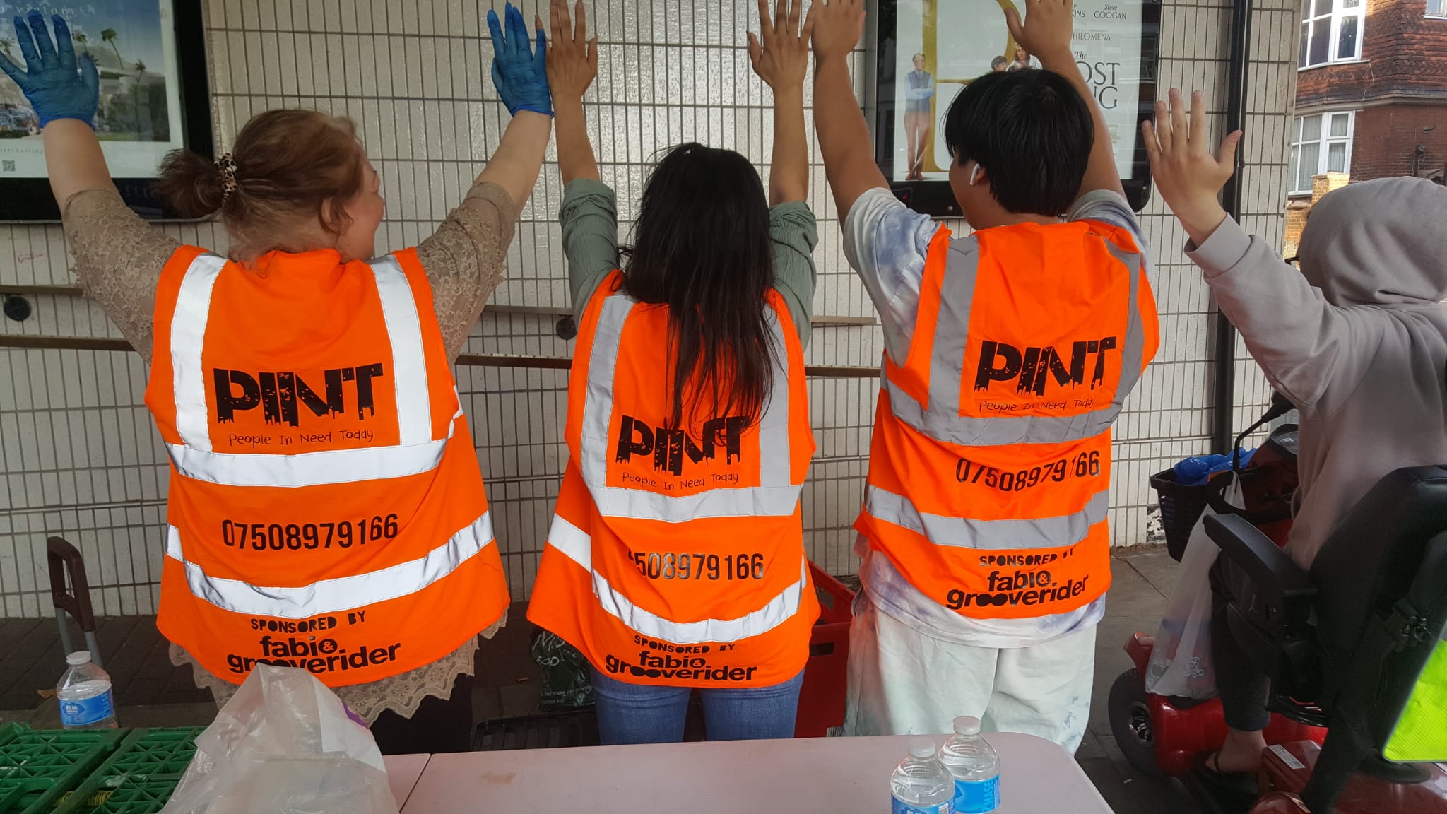 Volunteers holding their hands up wearing branded high-visibility vests