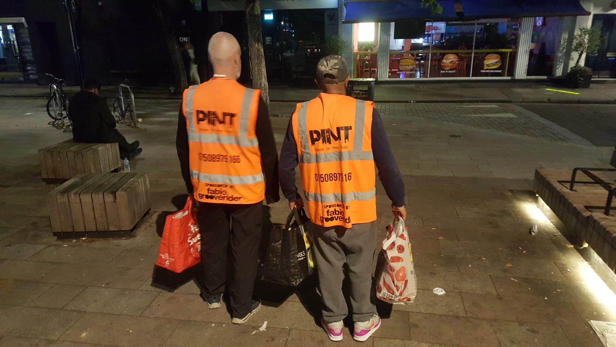 Photograph of volunteers facing away from the camera, showing the People In Need Today logo on their high-visibility jackets.